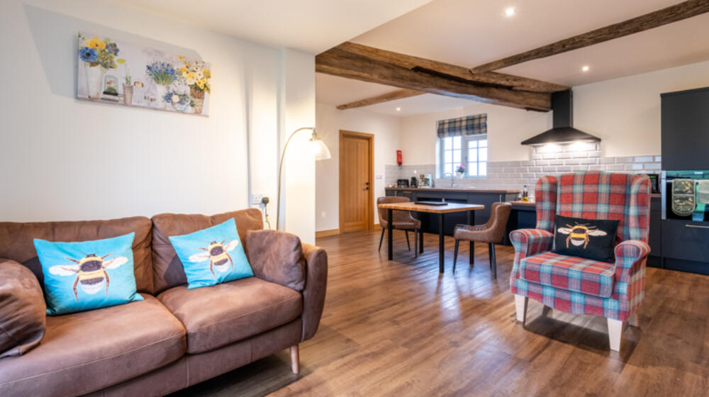 Accessible Living area, wood floor, leather sofa to the left, tartan chair, fitted kitchen behind in stiffkey blue, with handmade oak table.