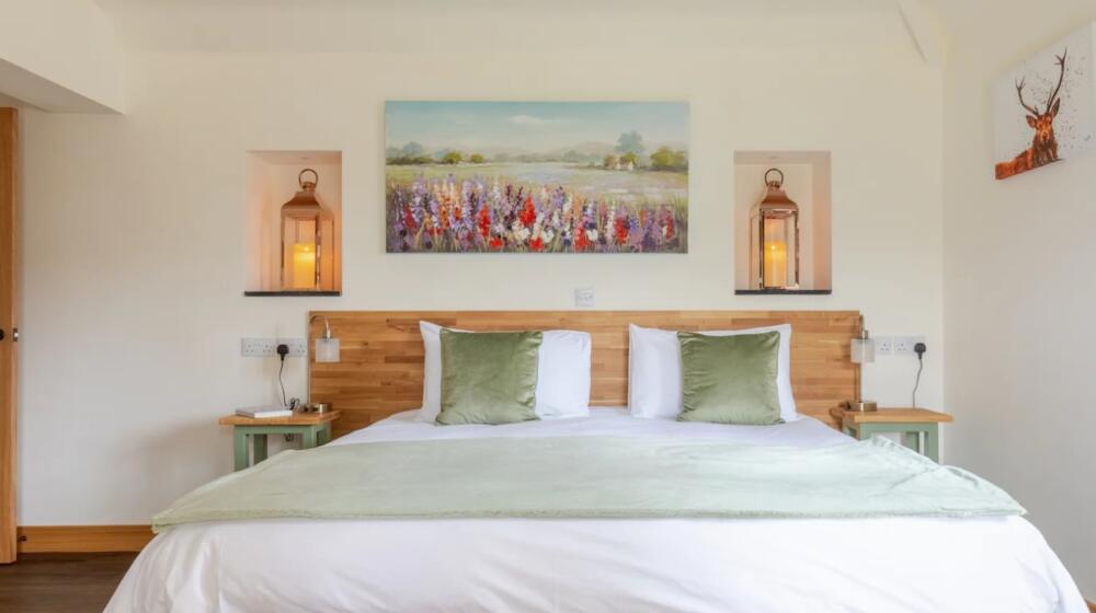 Accessible Master Bedroom in the Stables, Super King Bed with crisp cotton bed linen, lanterns in recesses each side of the bed, 4 sockets by each bedside table and pale green cushions.